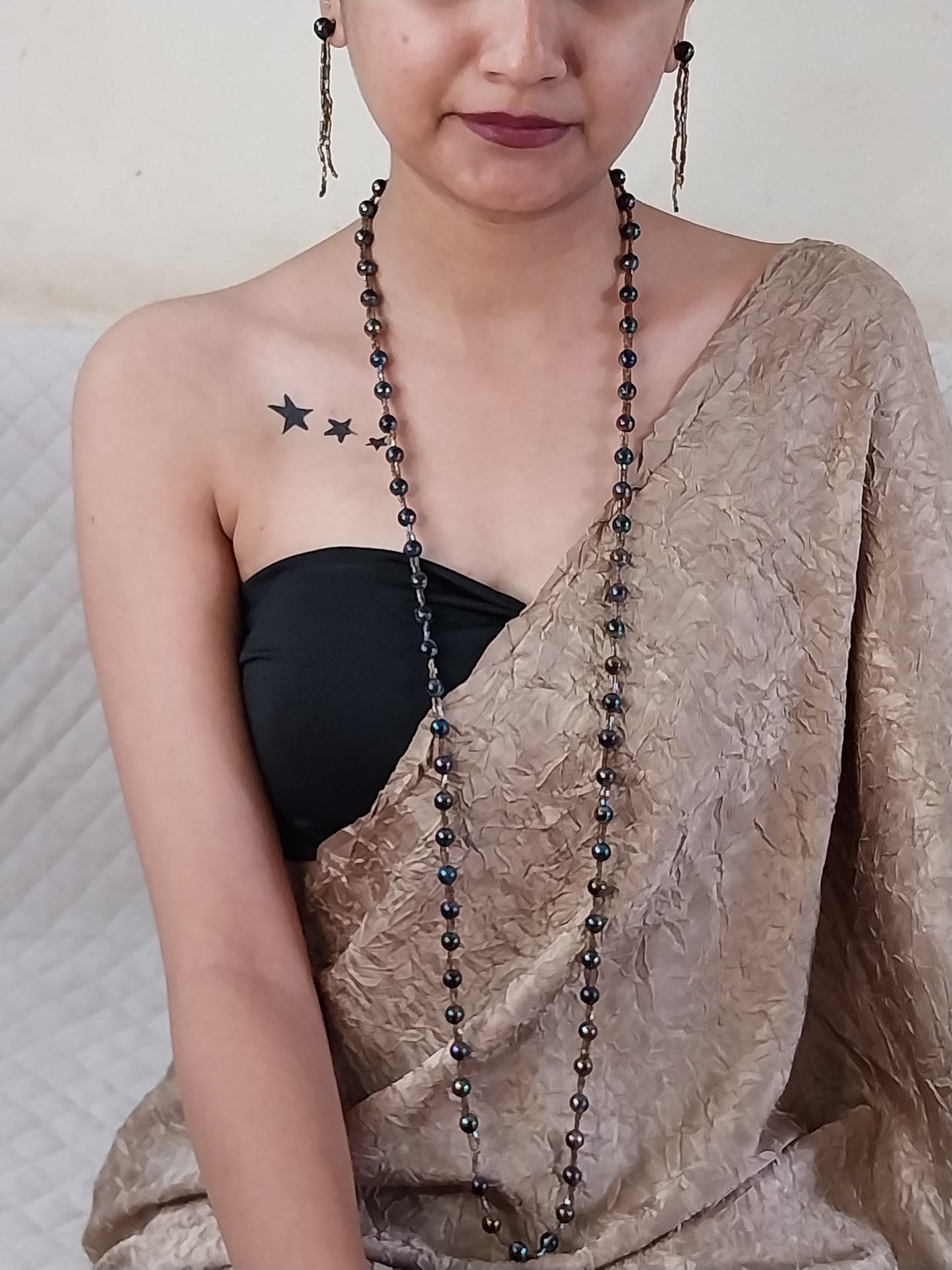 Person wearing a black top with visible tattoos on their arm, holding a beaded necklace.