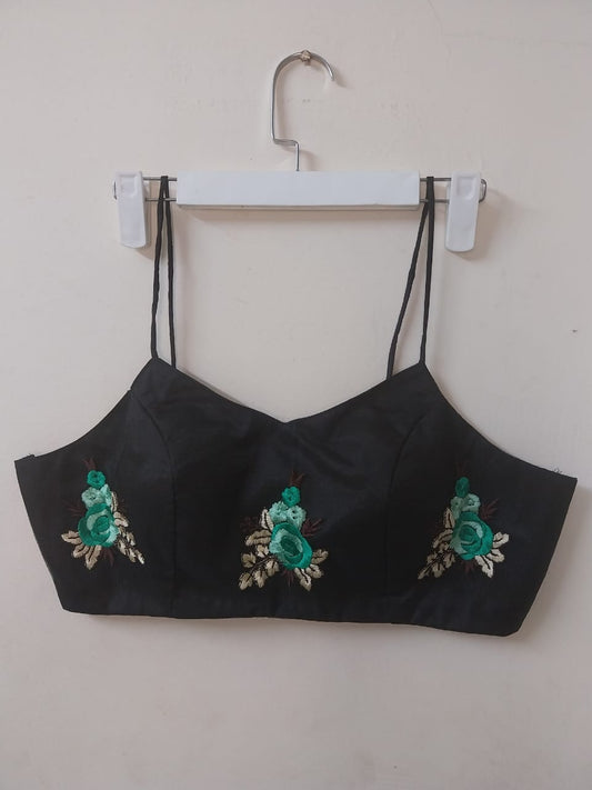 Black crop top with green floral embroidery on a white hanger against a white background