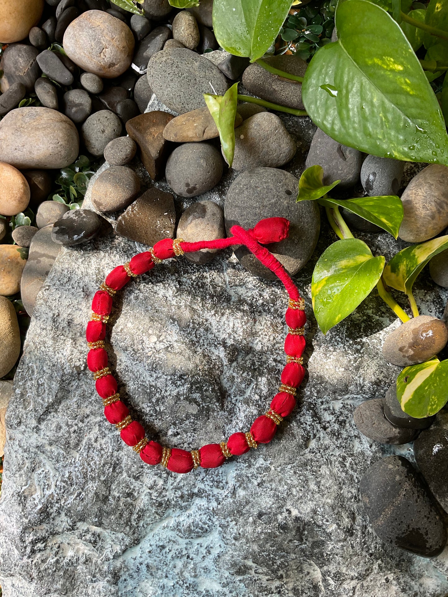 Red beaded bracelet on a rock with green leaves
