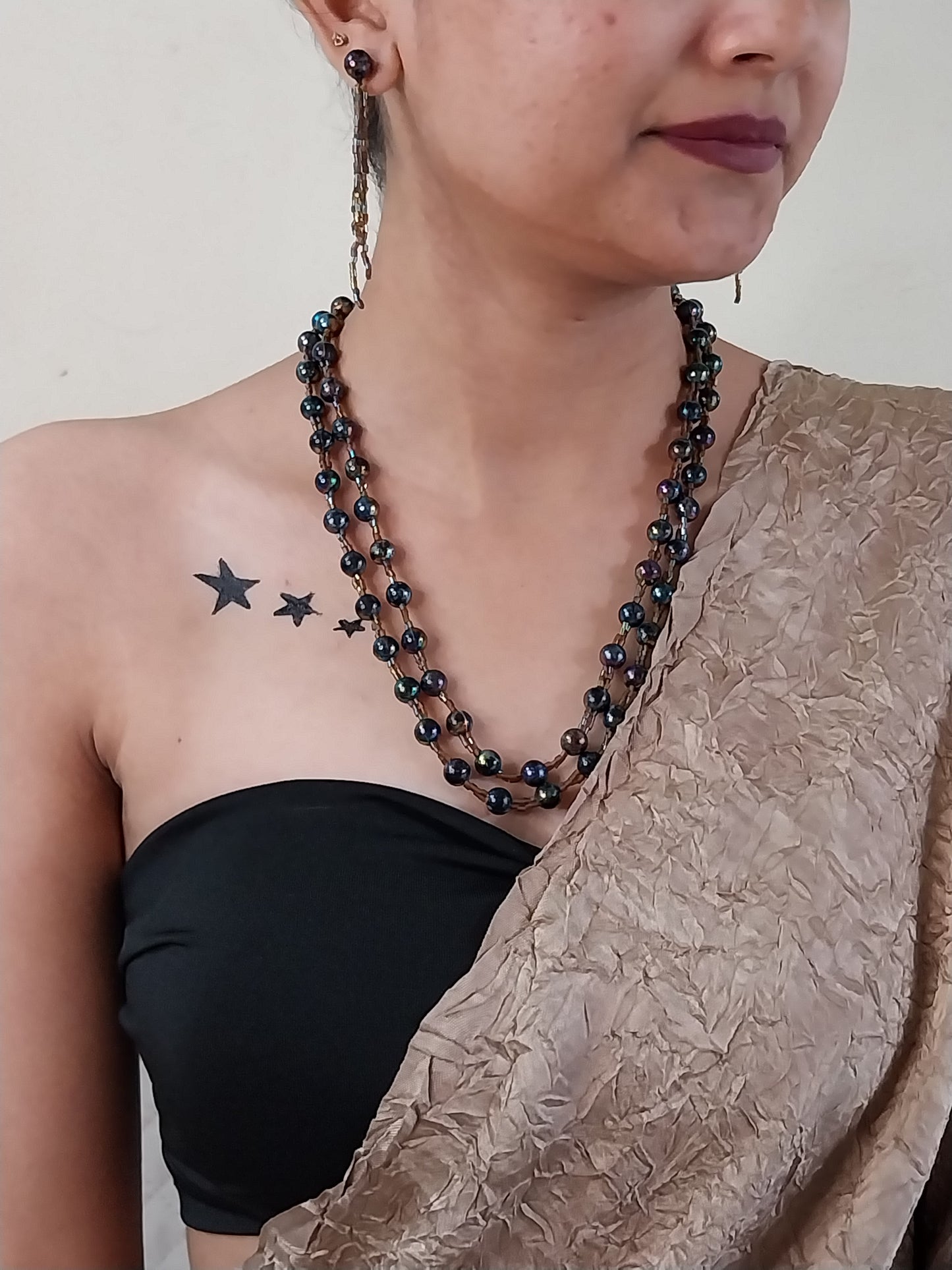Person wearing a black beaded necklace with a star tattoo on their chest.