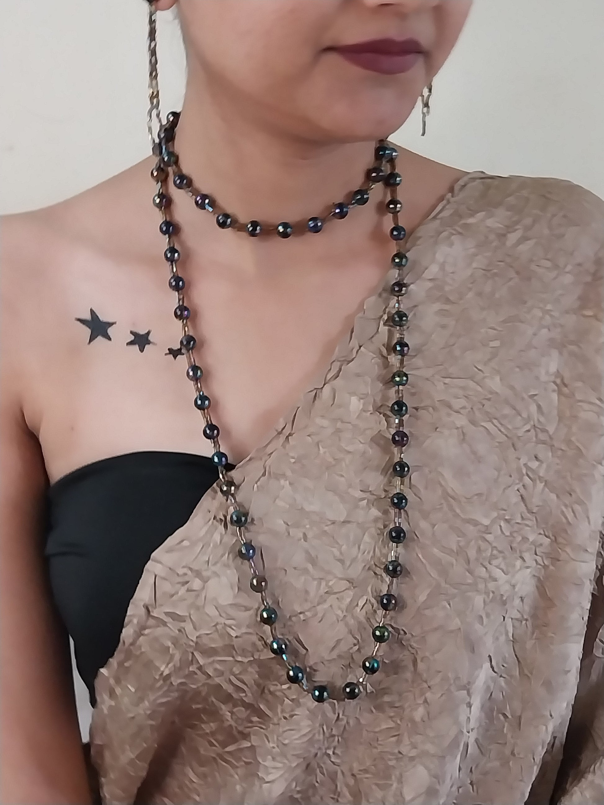 Person wearing a black beaded necklace with a star tattoo on their chest.
