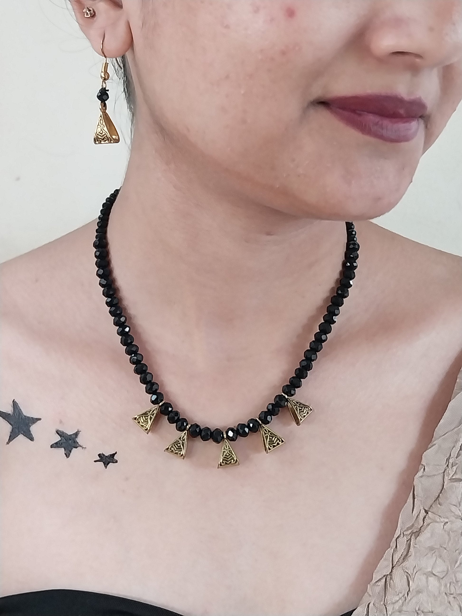Person wearing a black beaded necklace with gold accents on a neutral background