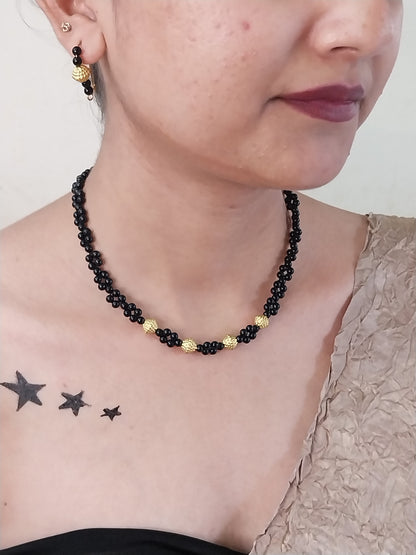 Close-up of a person wearing a black beaded necklace with gold accents, with star tattoos on the chest.