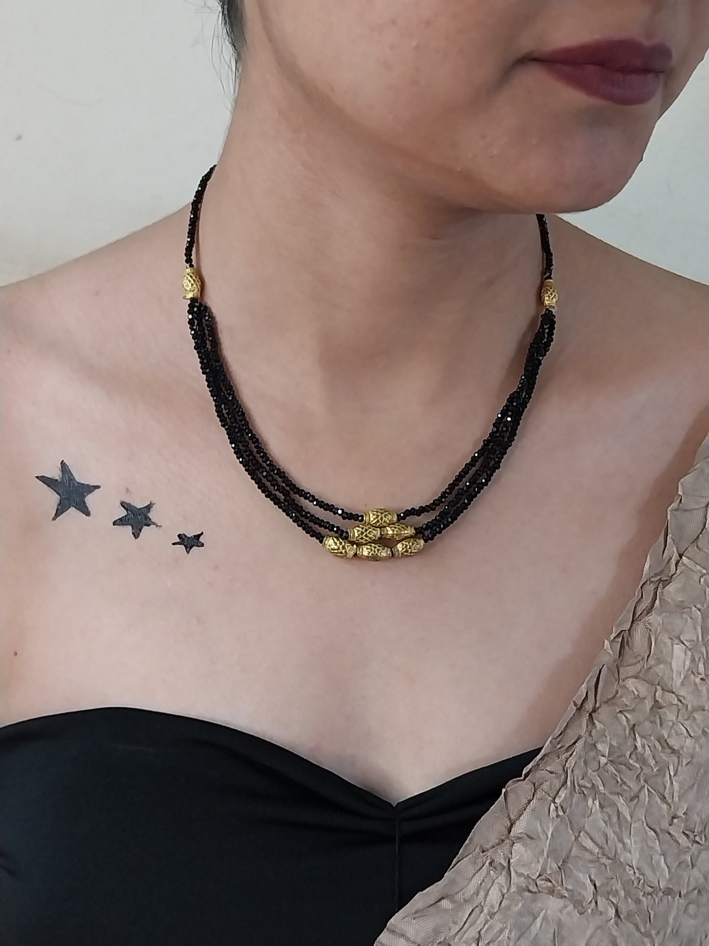 Person wearing a black beaded necklace with gold accents, with three star tattoos visible.