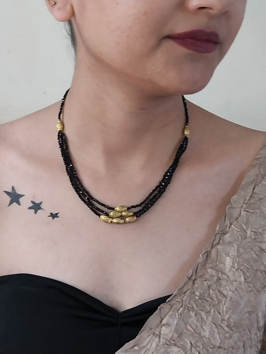 Person wearing a black beaded necklace with gold accents on a neutral background
