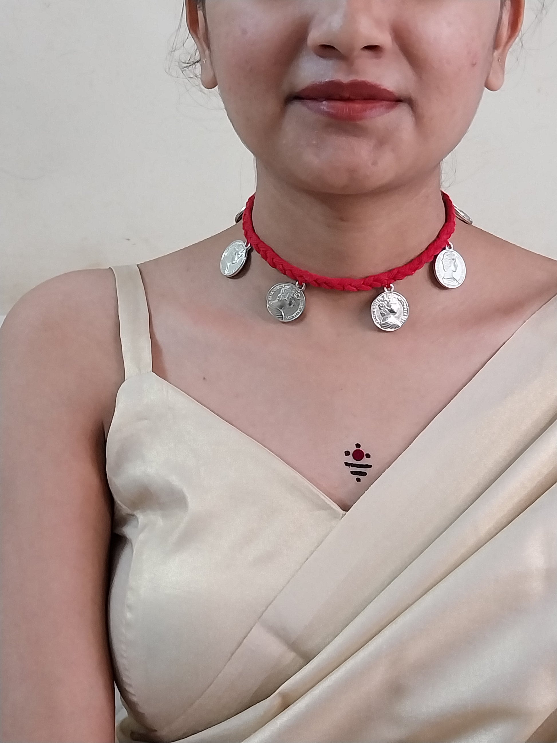 Close-up of a person wearing a red necklace with silver charms on a plain background
