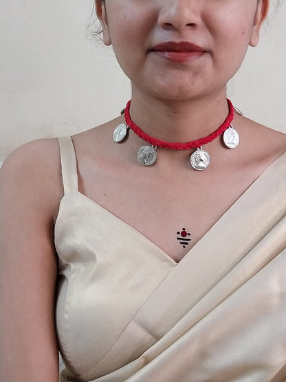 Close-up of a person wearing a red necklace with silver charms on a plain background