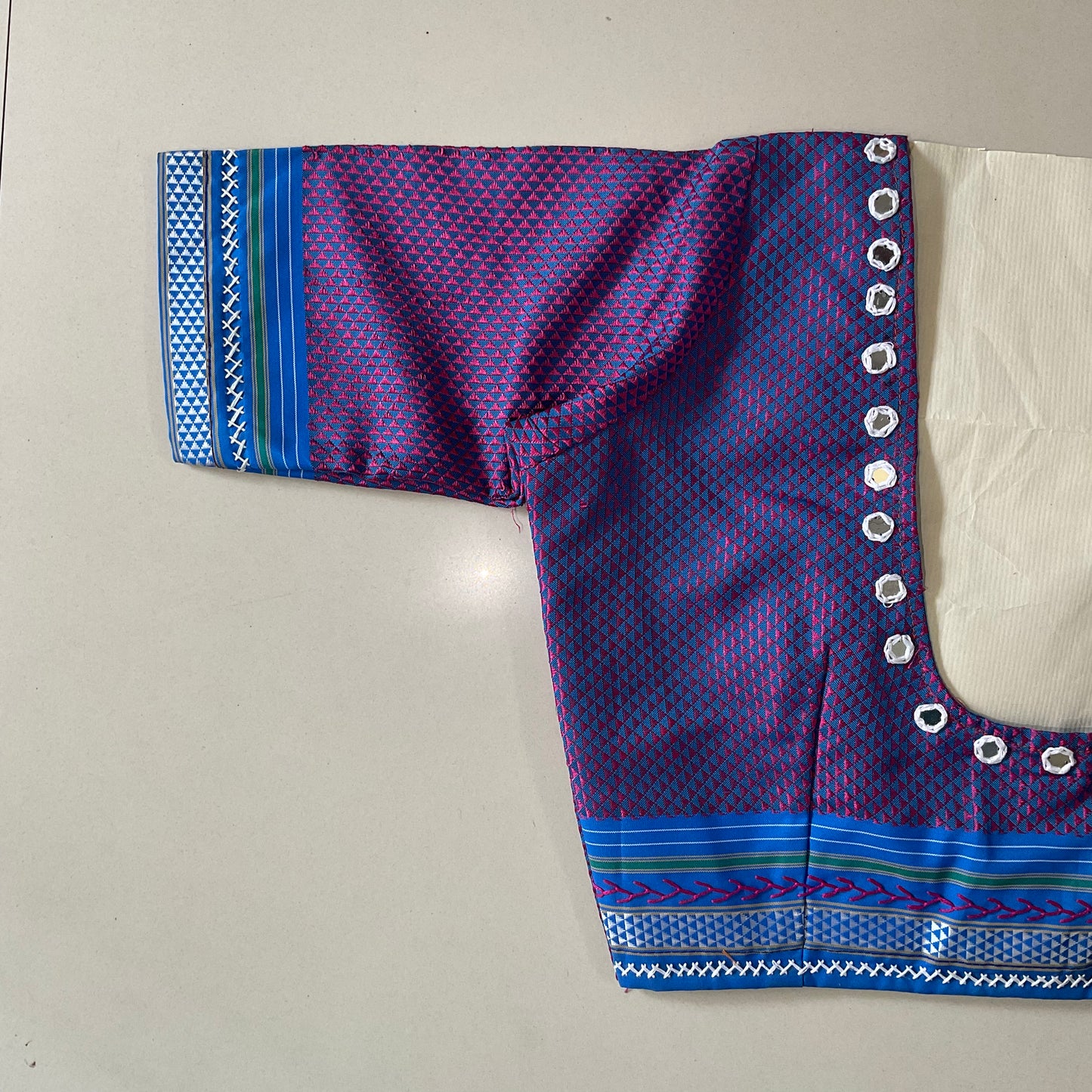 Purple and blue patterned blouse with decorative border on a light gray background