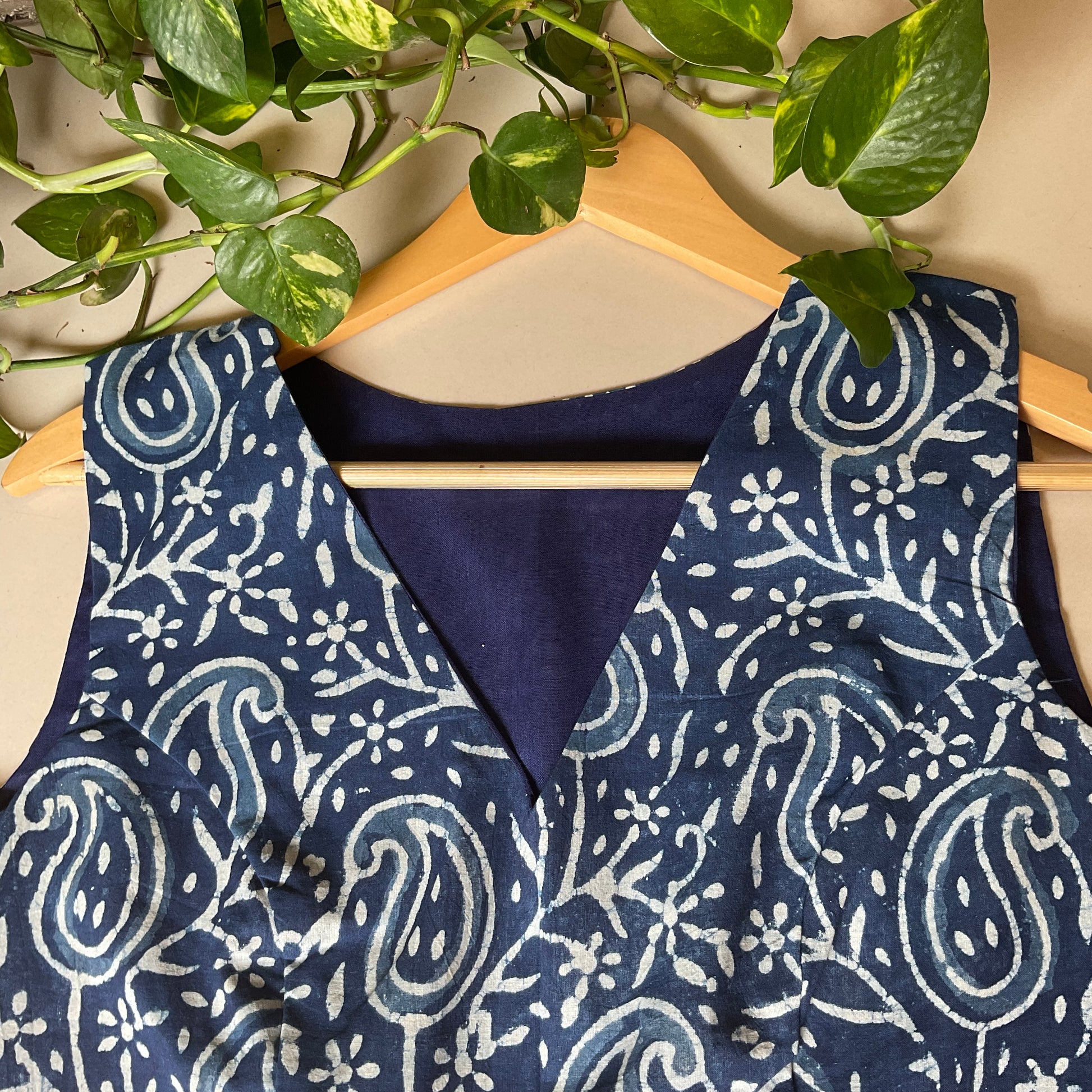 Indigo blouse with white paisley pattern on a wooden hanger against a neutral background.