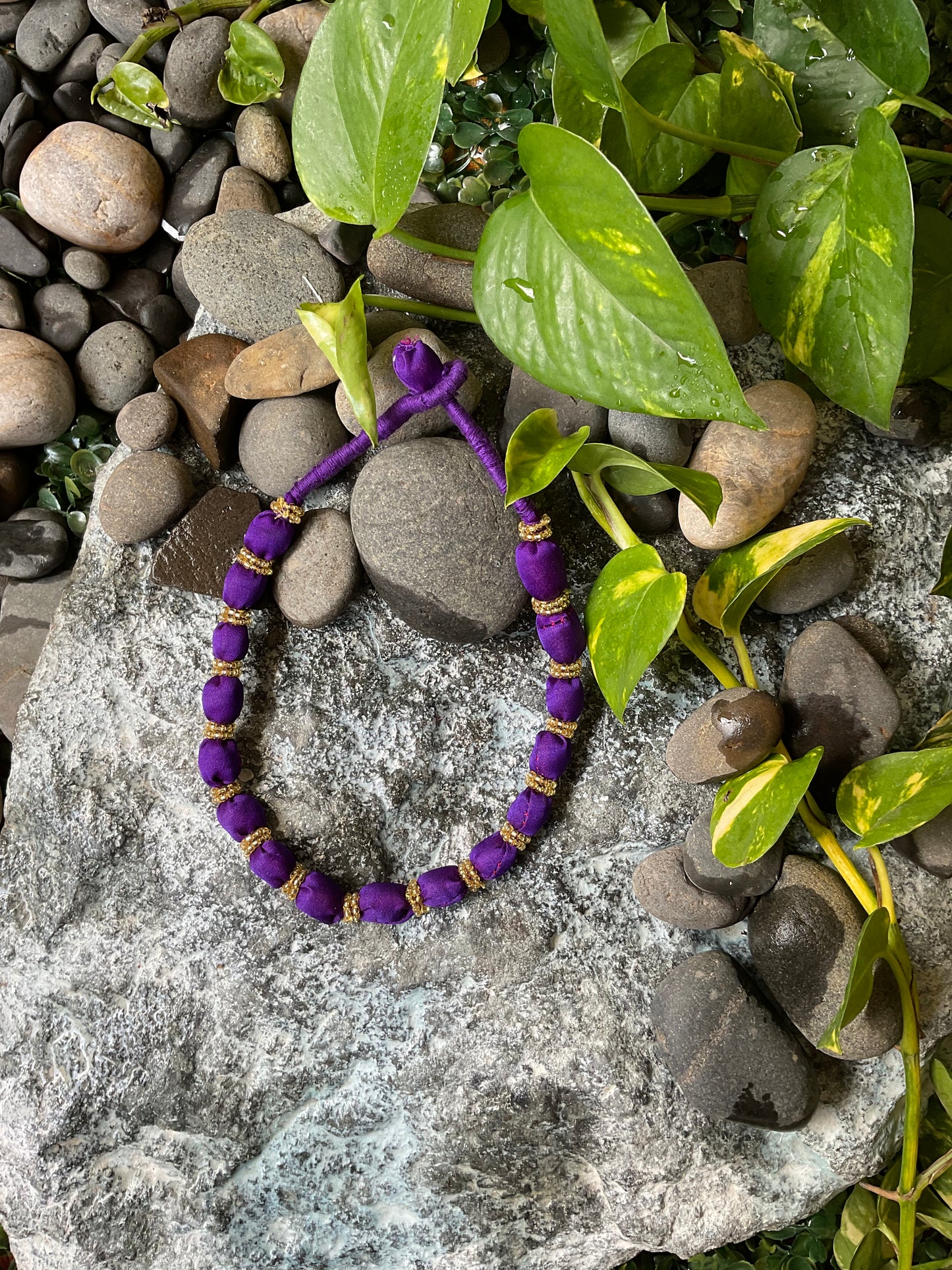 Purple beaded bracelet on a stone surface with green leaves