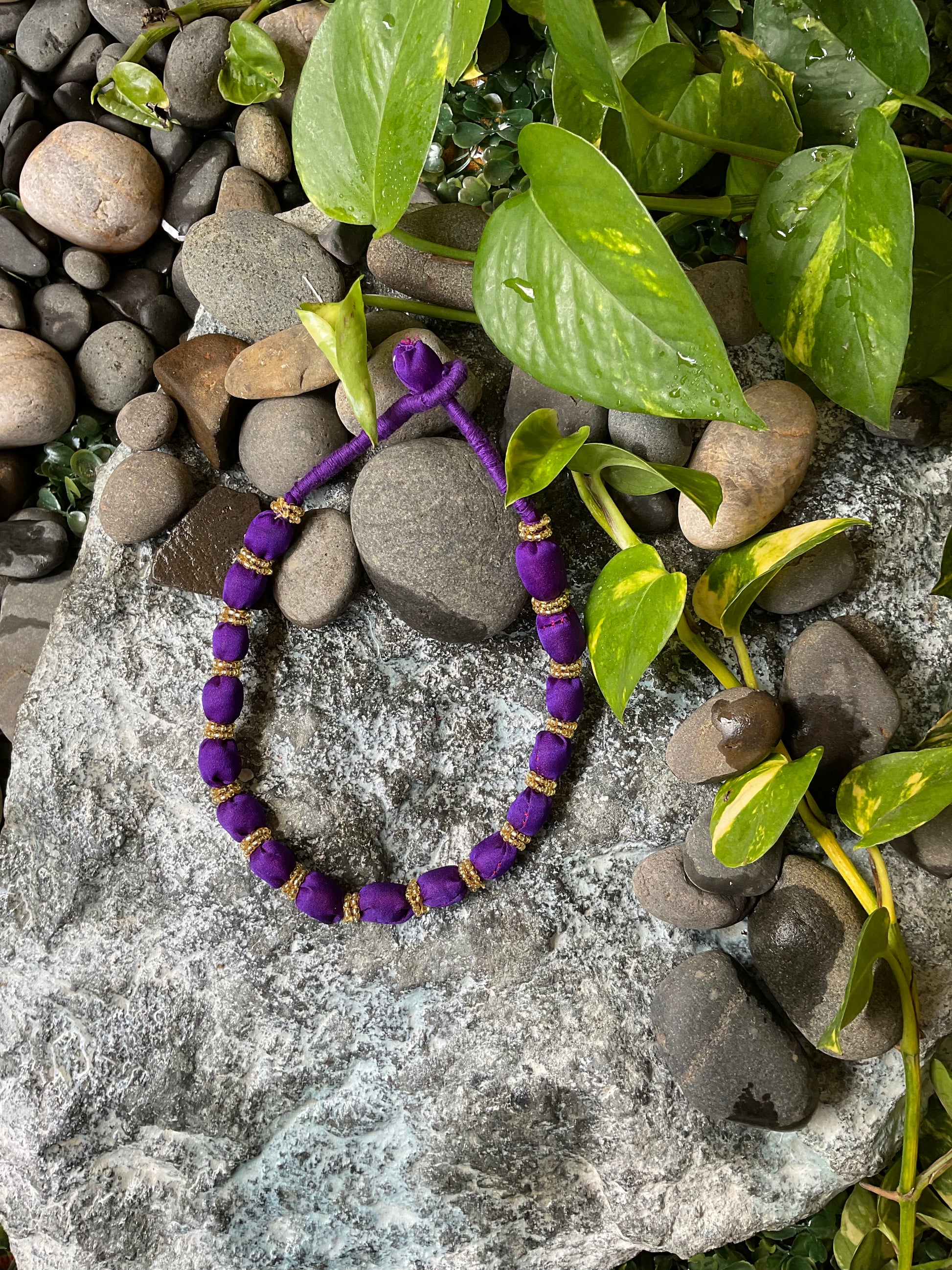 Purple beaded bracelet on a stone surface with green leaves