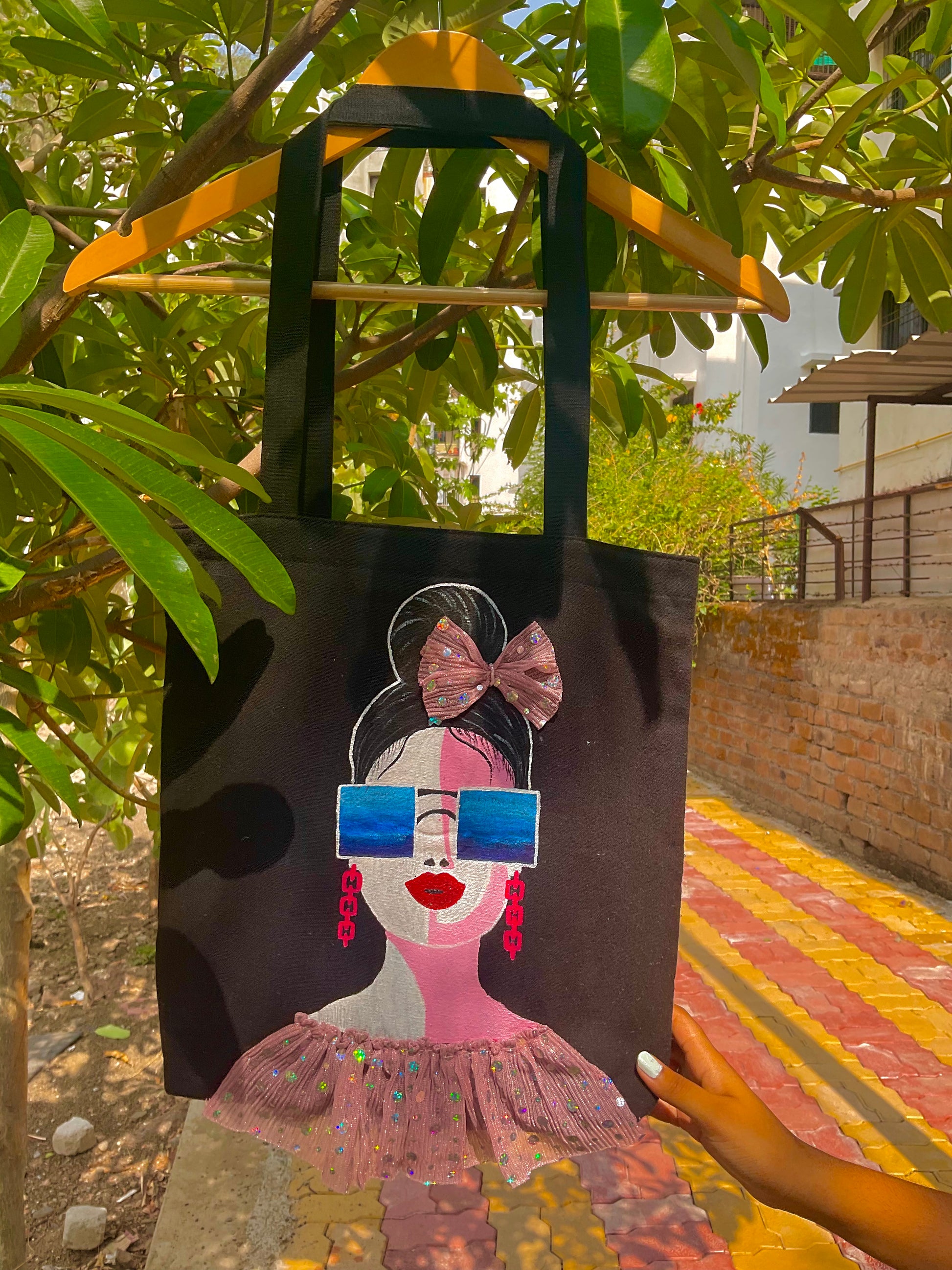 Tote bag with a stylized illustration of a woman wearing sunglasses and a pink dress, held by a person outdoors.