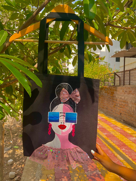 Tote bag with a stylized illustration of a woman wearing sunglasses and a pink dress, held by a person outdoors.