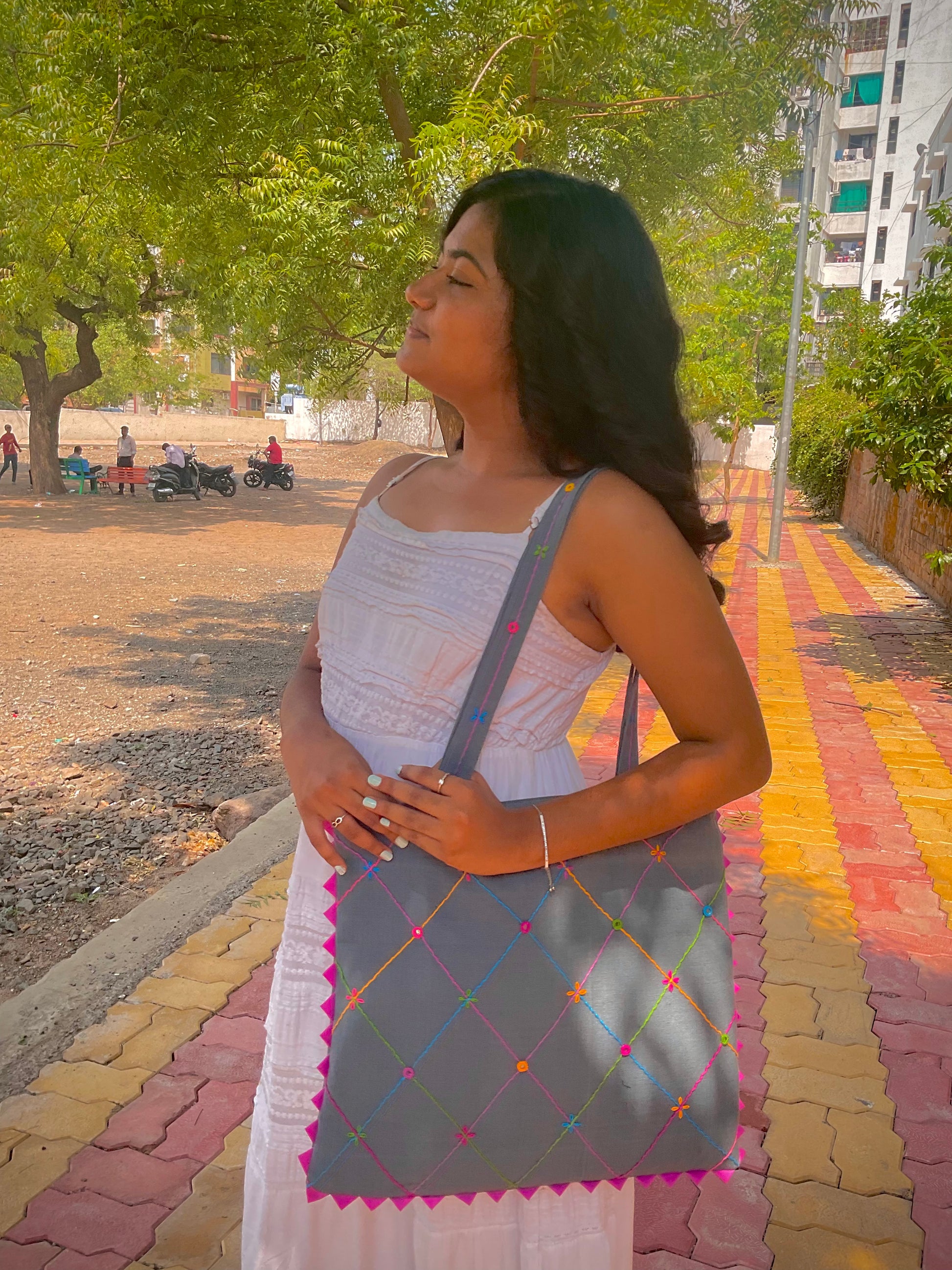 Woman holding a gray bag on a colorful pathway with trees and buildings in the background