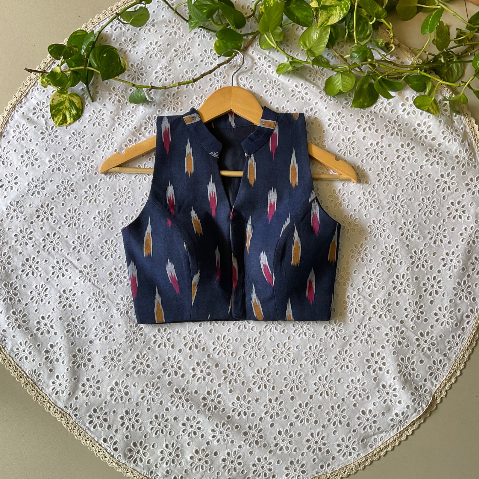 Navy blue blouse with a feather pattern on a wooden hanger against a white lace background