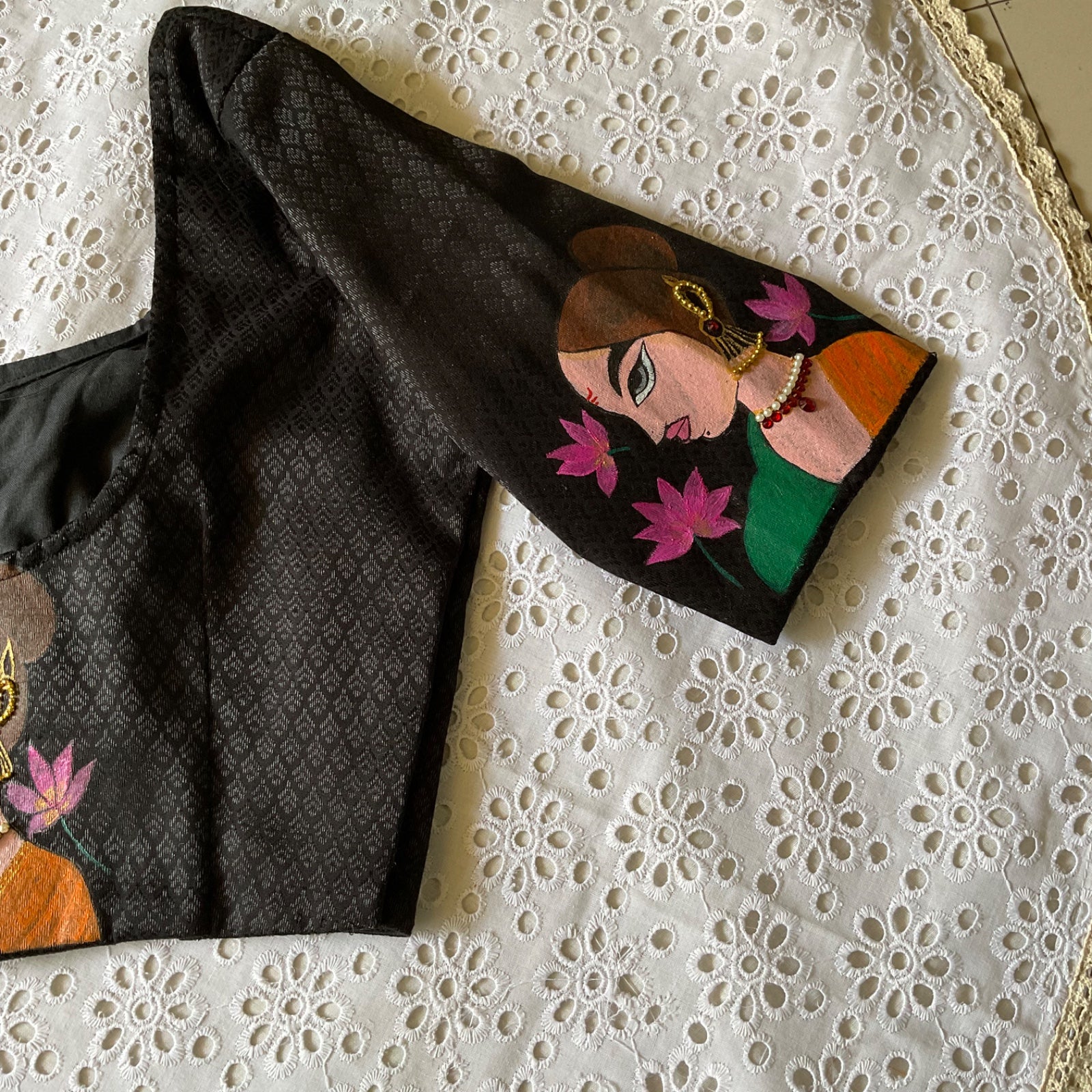 Black blouse with a colourful design of a woman and flowers on a white lace background
