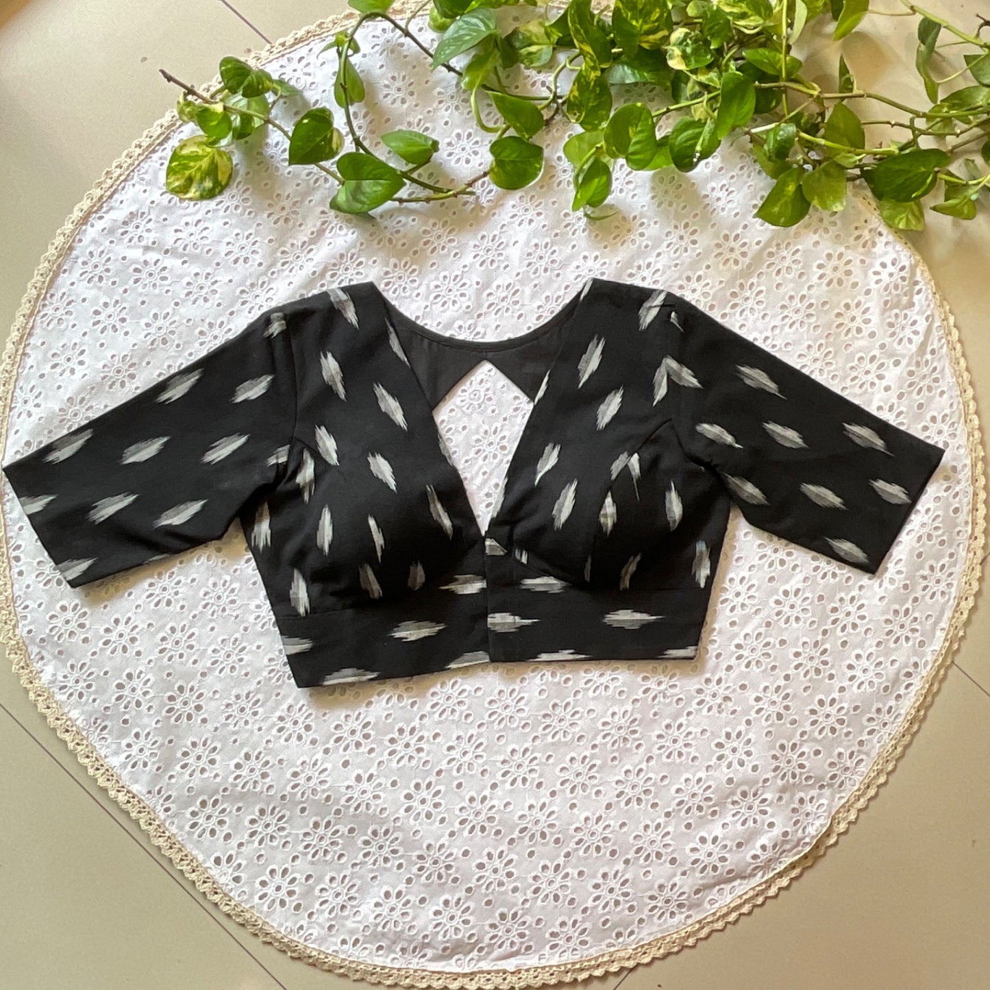 Black patterned blouse on a white lace surface with green leaves.