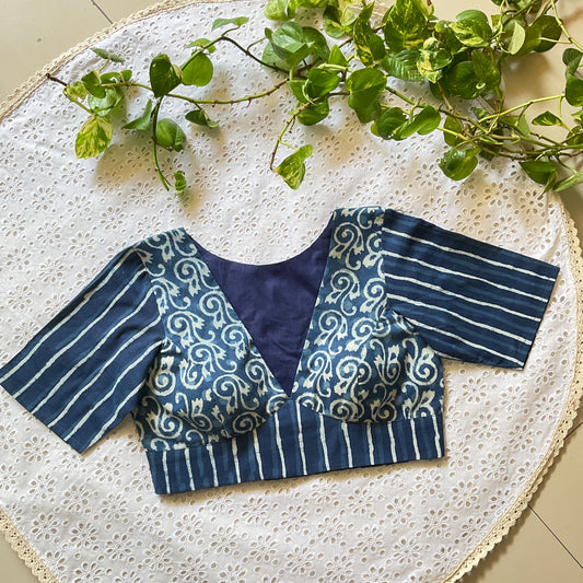 Blue and white patterned blouse on a textured surface with green leaves.