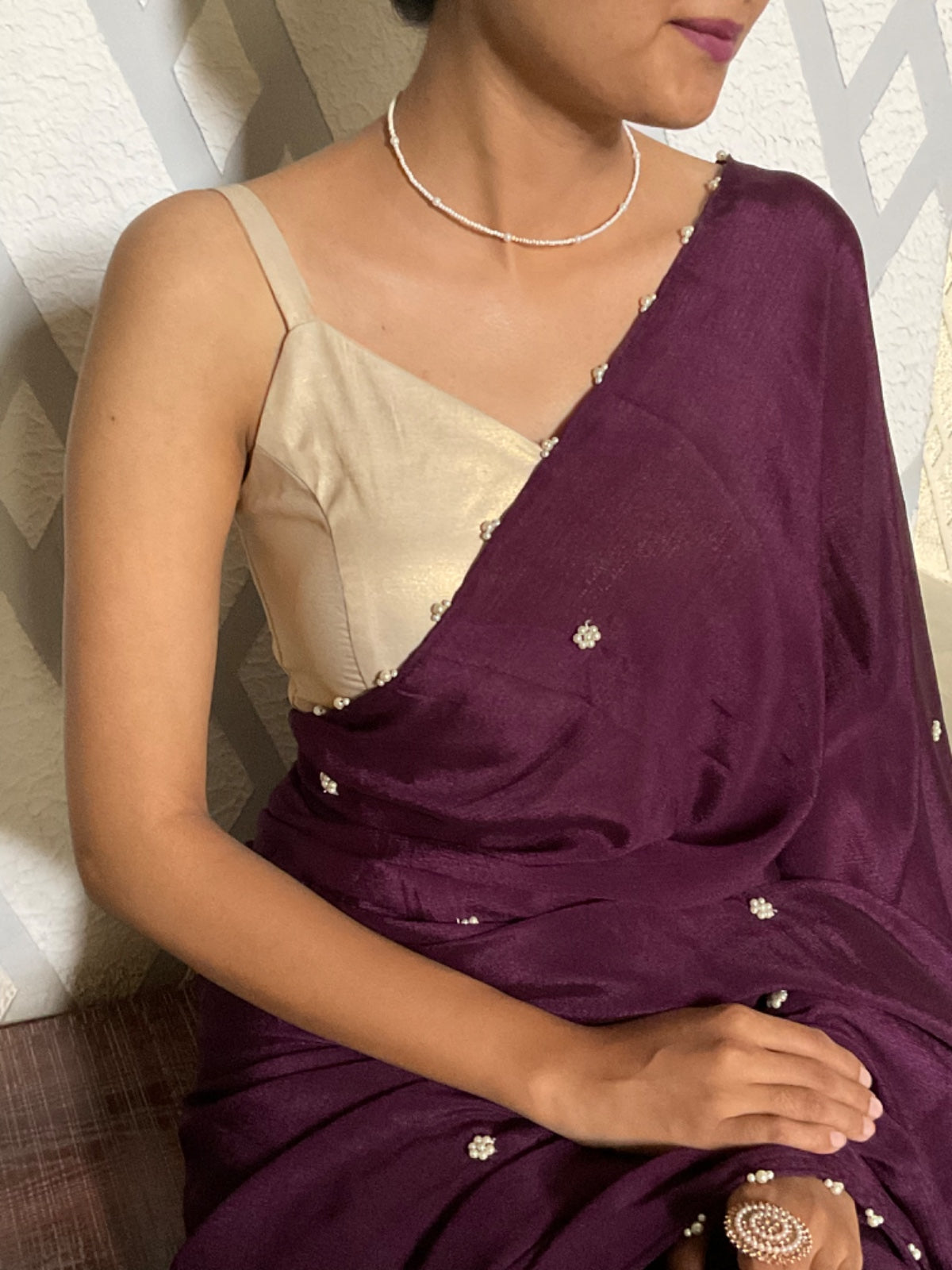 Woman wearing a purple saree with a beige blouse, sitting against a neutral background.