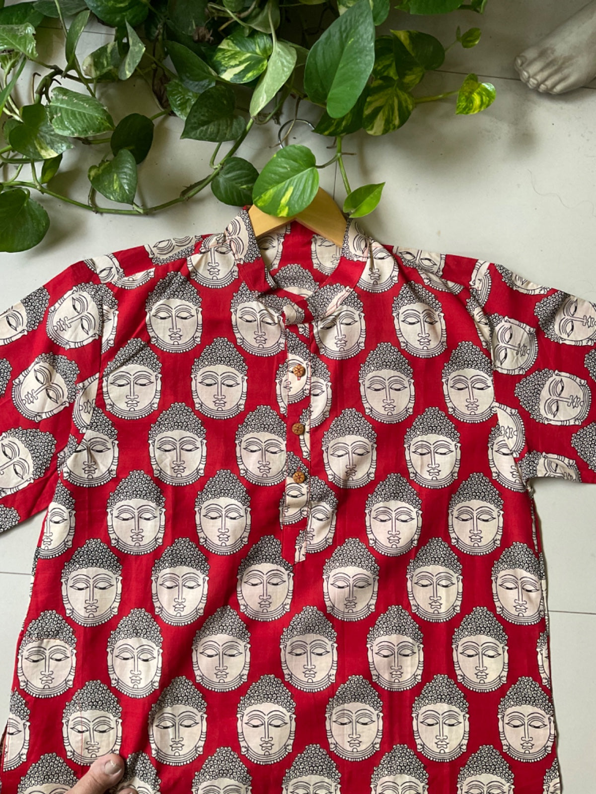Red kurta with silver Buddha patterns on a white surface with green leaves.