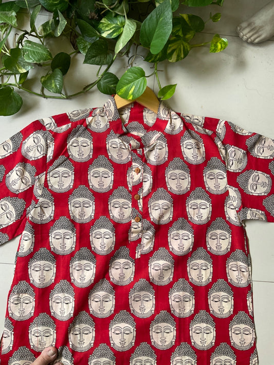 Red kurta with silver Buddha patterns on a white surface with green leaves.