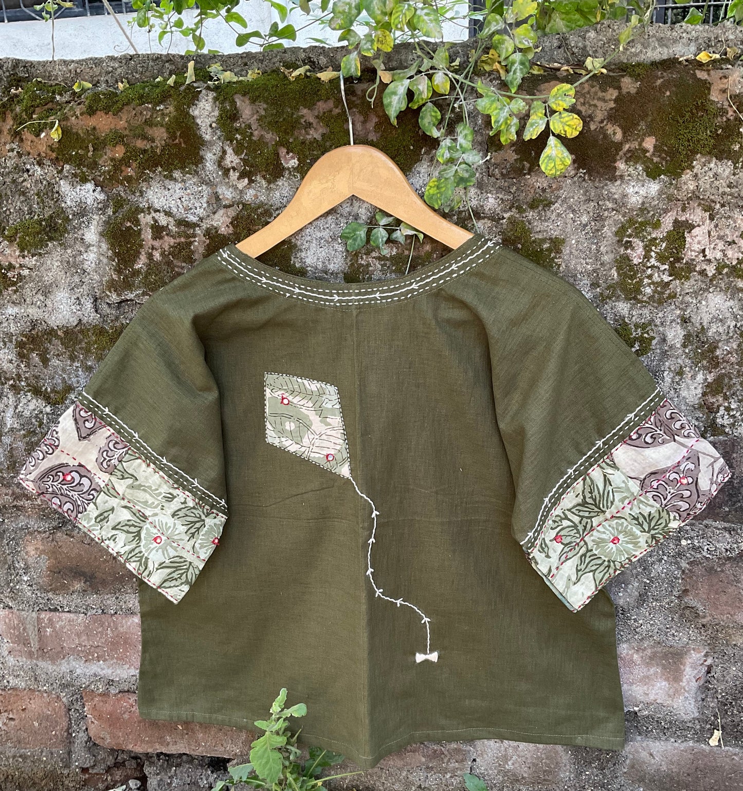 Green dress with floral patterns on a hanger against a textured wall.