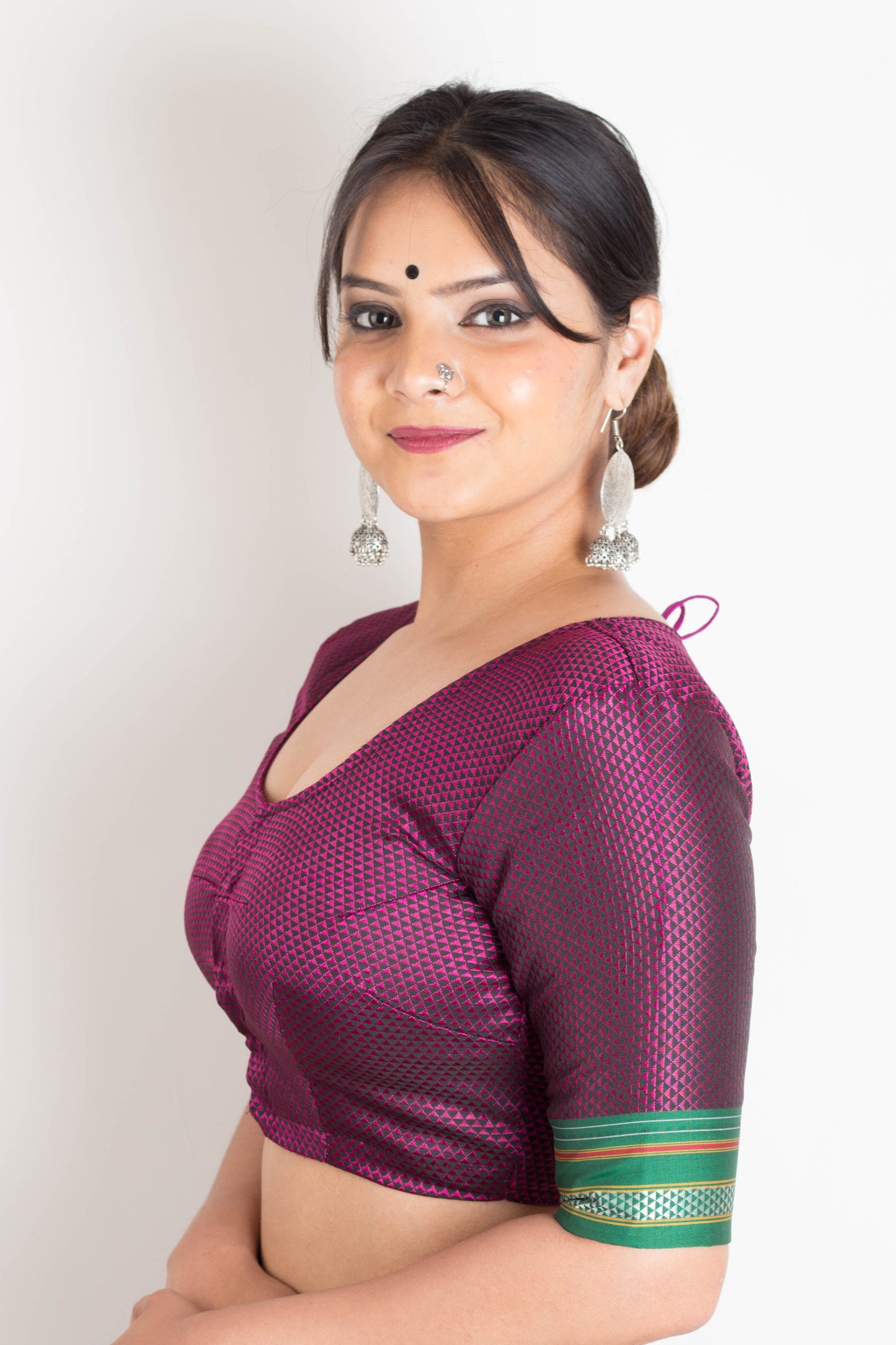 Woman wearing a purple blouse with green accents and blue jeans against a white background