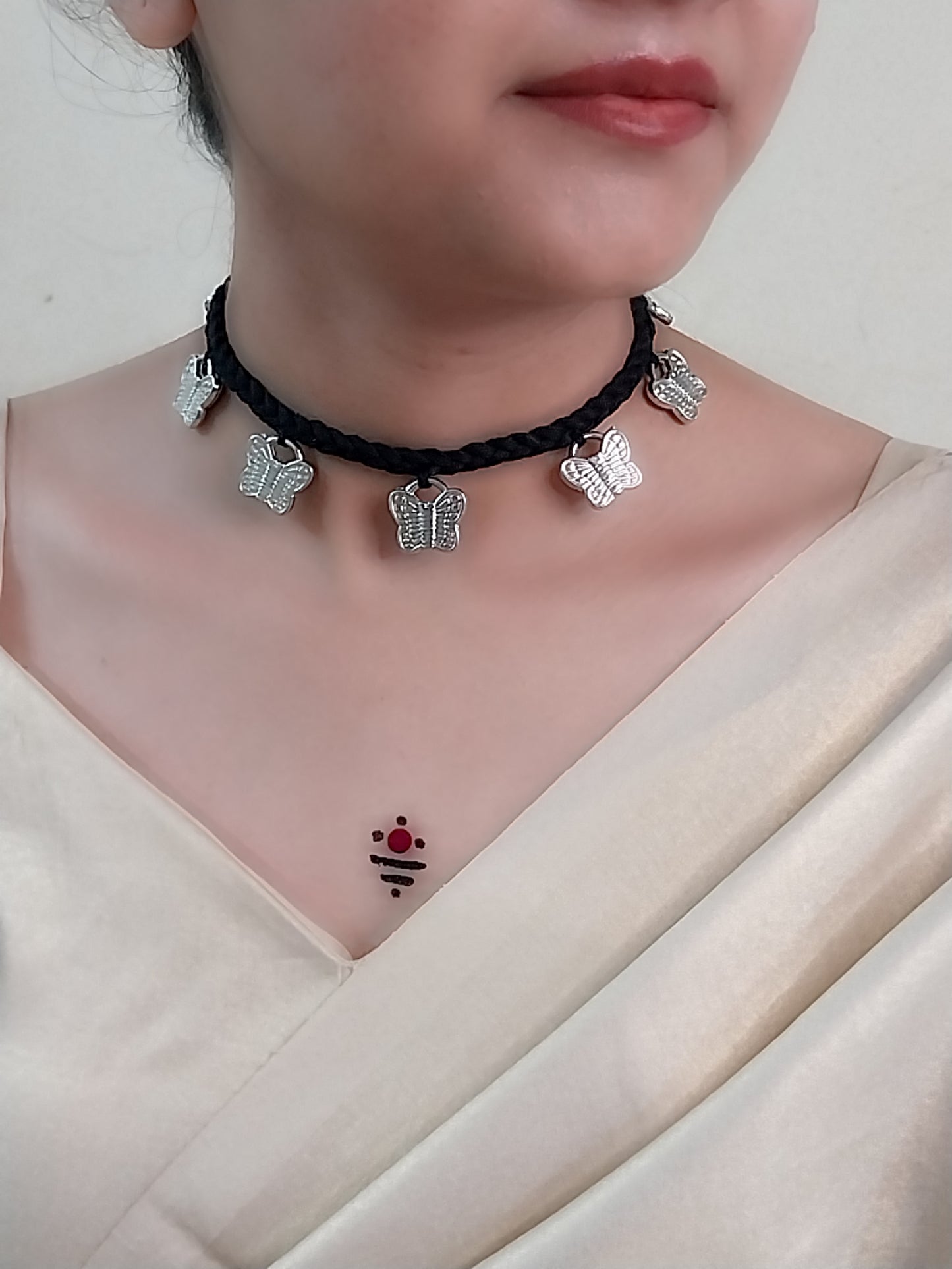 Person wearing a black choker necklace with butterfly charms on a plain background