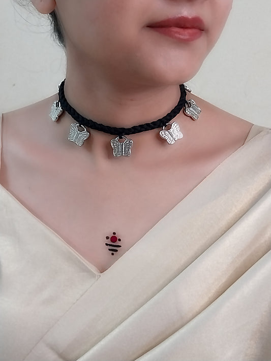 Person wearing a black choker necklace with butterfly charms on a plain background