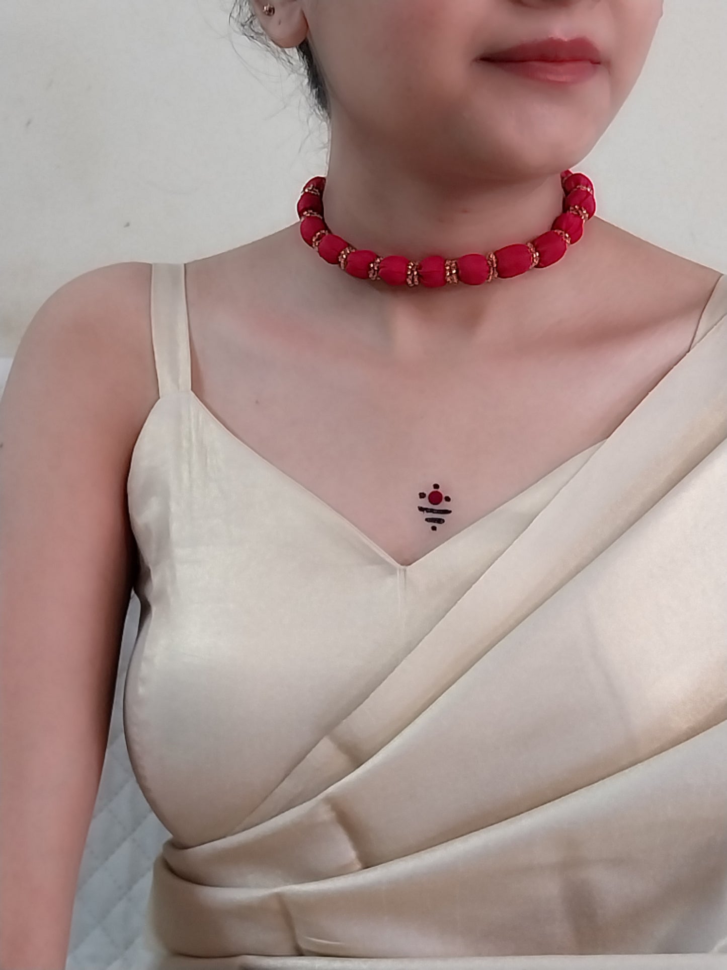A person wearing a red beaded necklace and a beige saree.