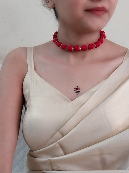 A person wearing a red beaded necklace and a beige saree.