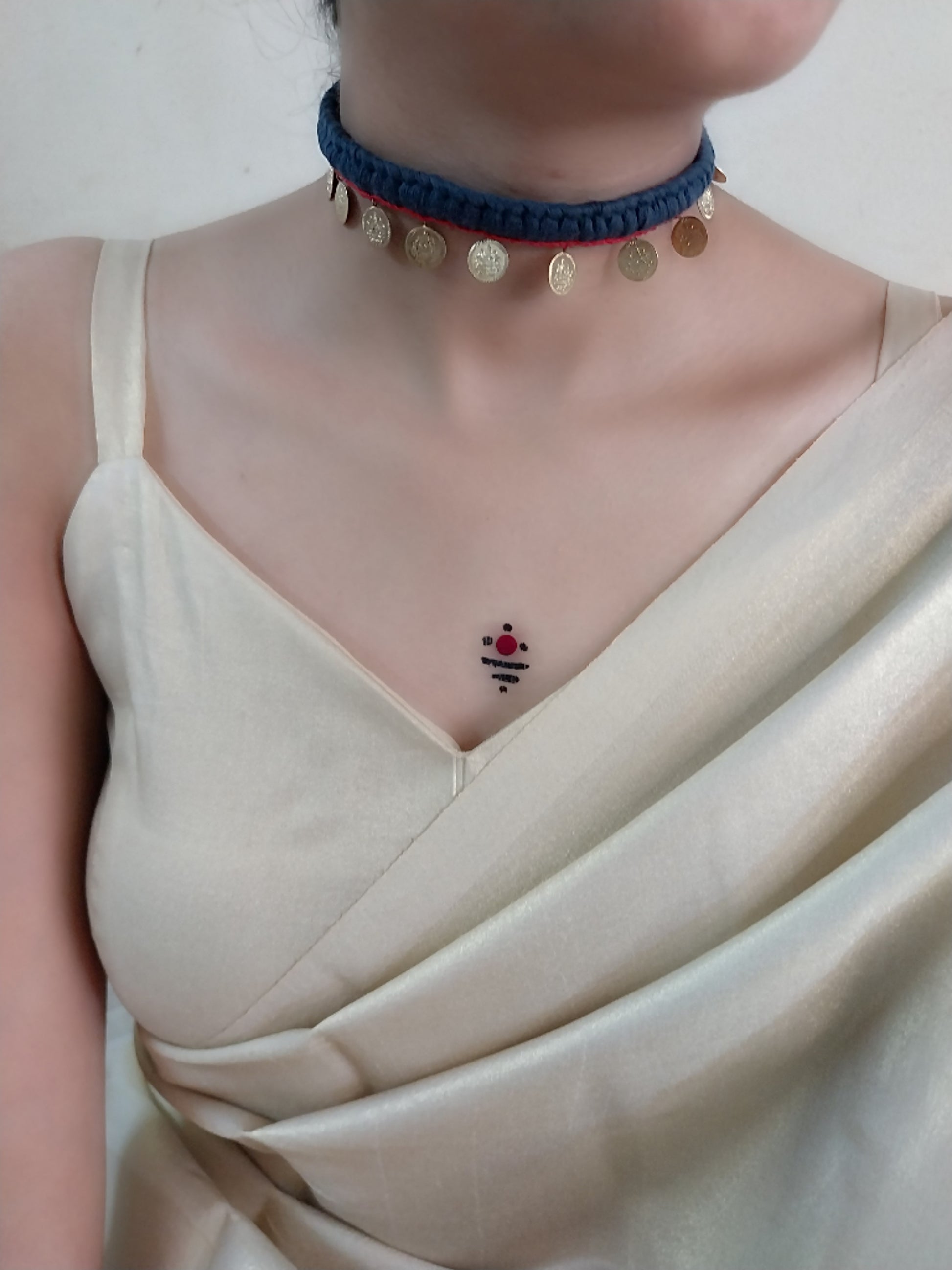 A person wearing a black choker necklace with golden details and circular pendants, paired with a light-colored top.