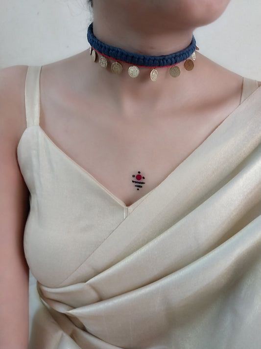 A person wearing a black choker necklace with golden details and circular pendants, paired with a light-colored top.