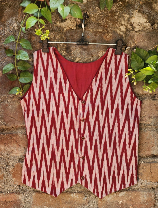 Red and white ikkat vest hanging on a brick wall with greenery.