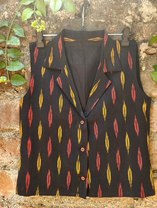 Black patterned vest on a hanger against a textured wall.