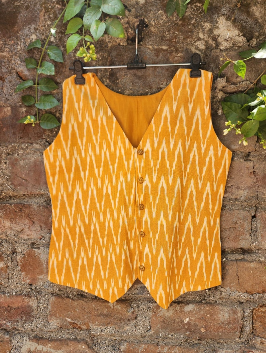 Yellow patterned vest hanging on a brick wall with greenery.